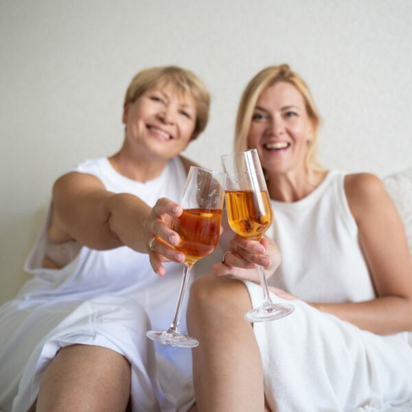 young-woman-with-mom-drinking-wine-while-sitting-on-bed